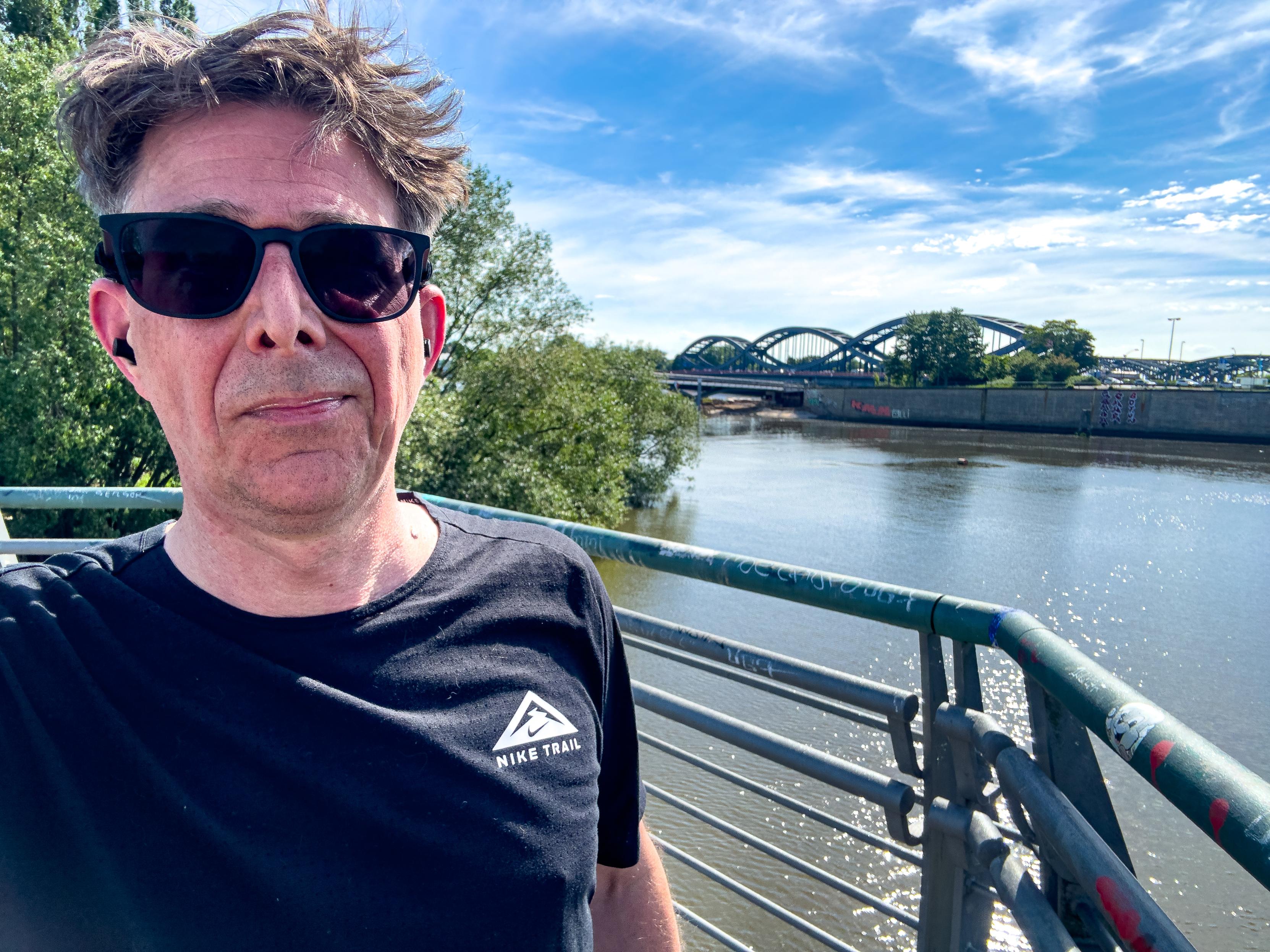 Ich mit Sonnenbrille vor einem Geländer. Im Hintergrund die Elbe und die Elbbrücken.